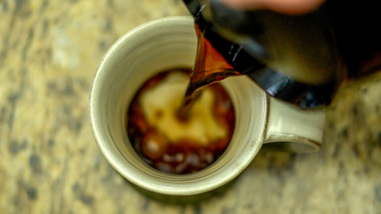 Seen from above, a dark liquid is pouring into a tea mug.