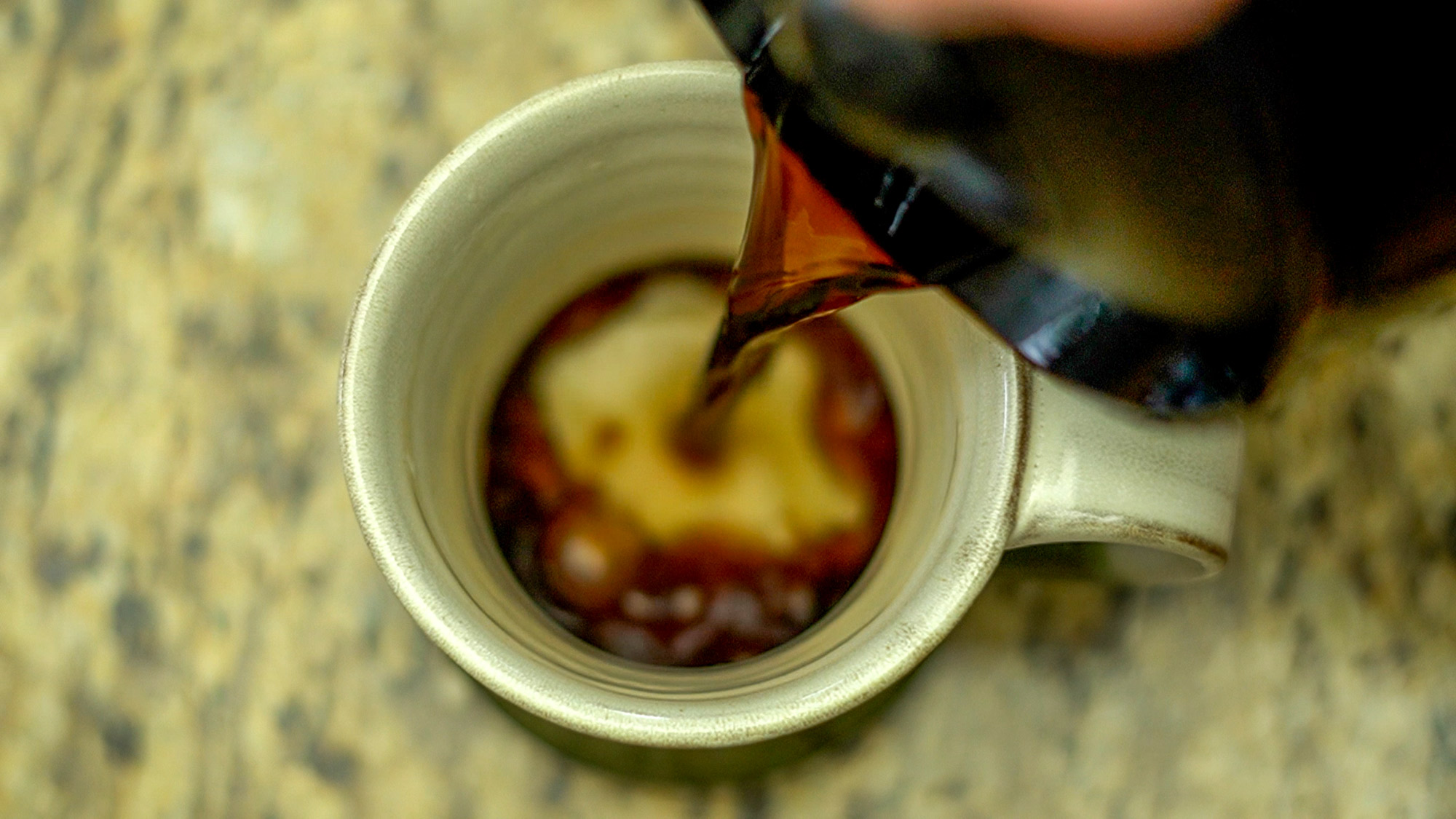Seen from above, a dark liquid is pouring into a tea mug.