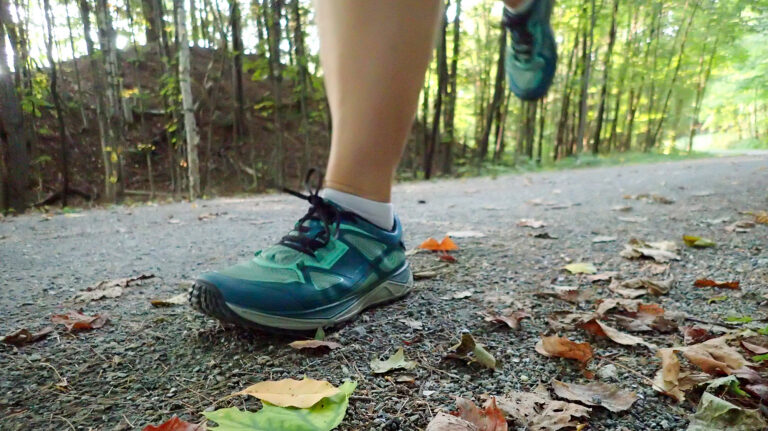 A close view of a person's running shoes on a gravel path in the fall.