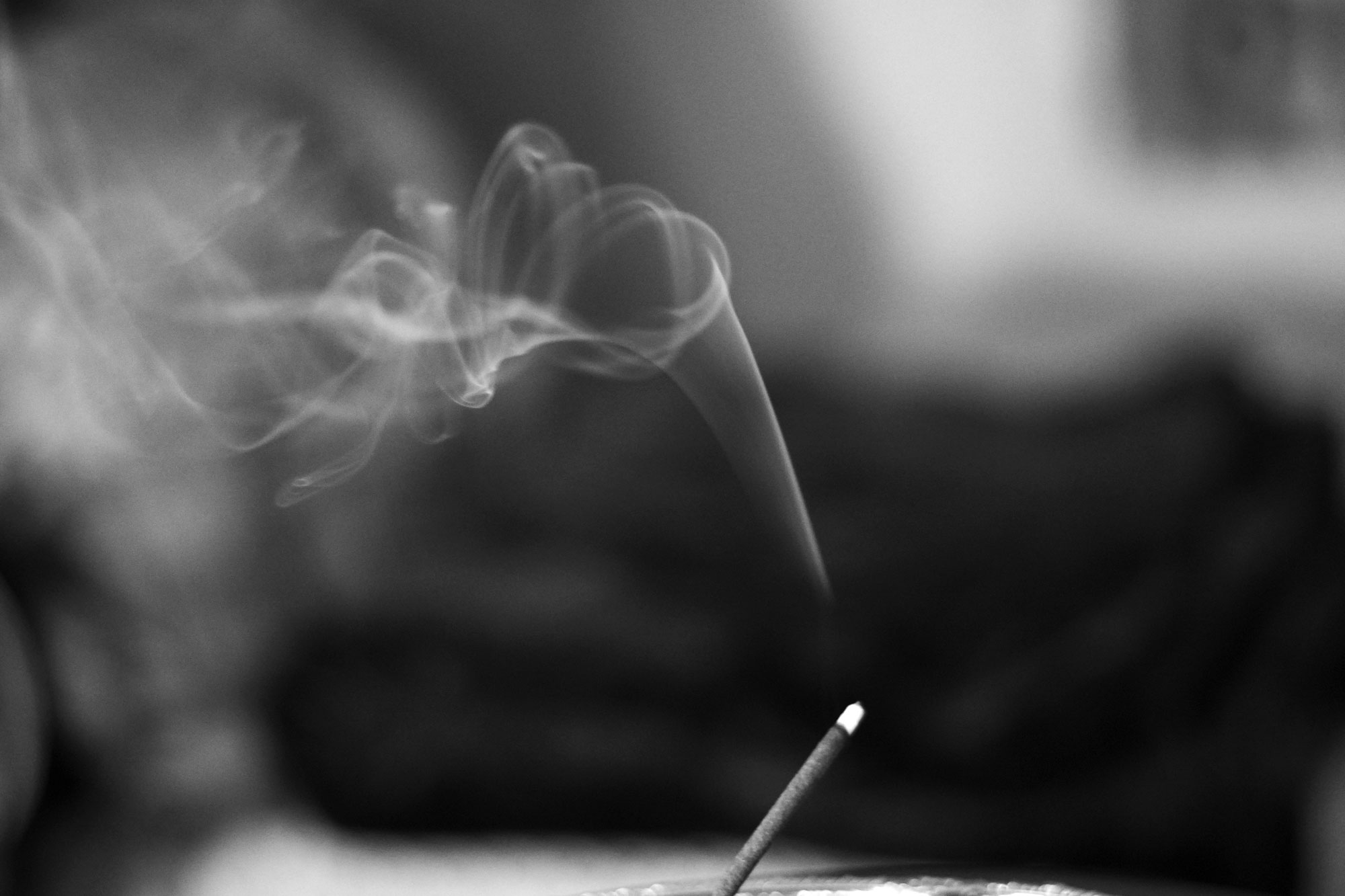 The smoke from burning incense billows in a black and white image.