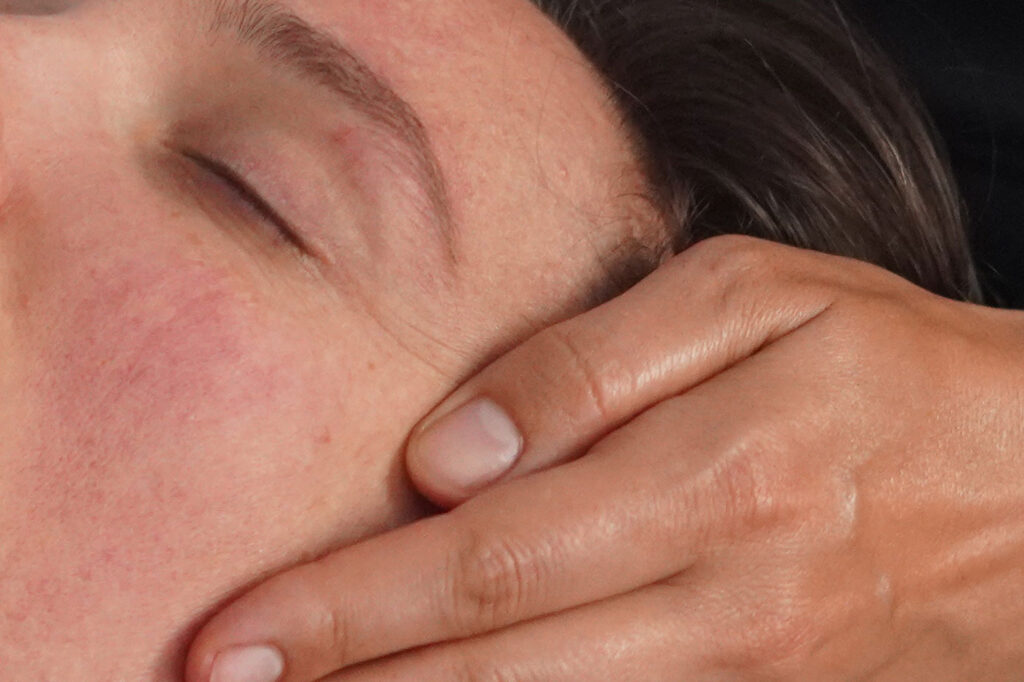 A close perspective of a person's face, lying face up, with a hand gently cradling the face. 